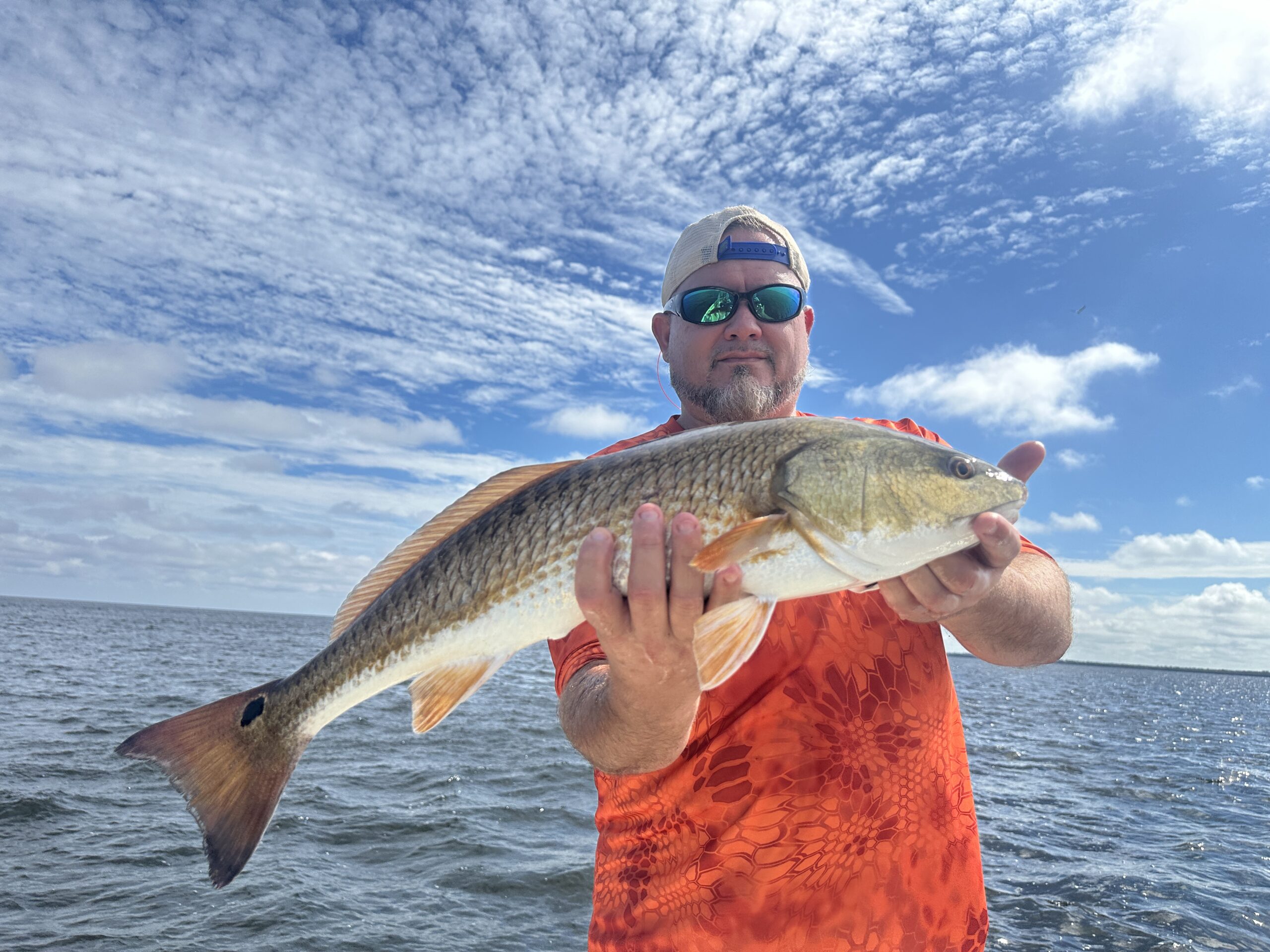 An angler in sunglasses holding up a redfish on Tampa Bay