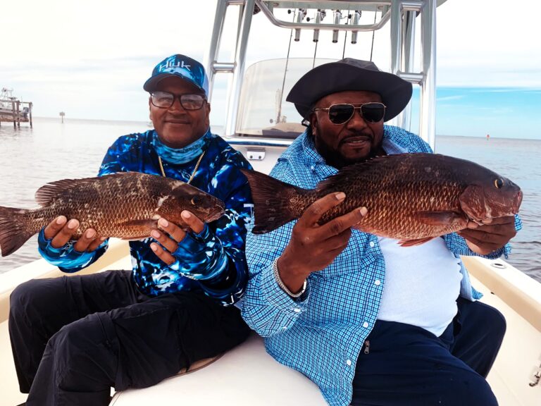 Two anglers holding mangrove snapper aboard the boat