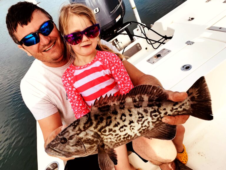 A father and daughter holding a grouper aboard the boat