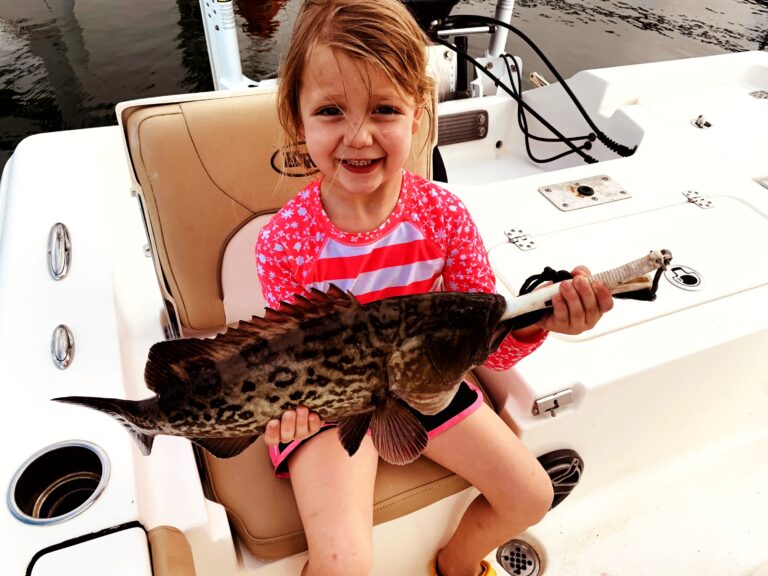 A young girl holding a grouper aboard the boat