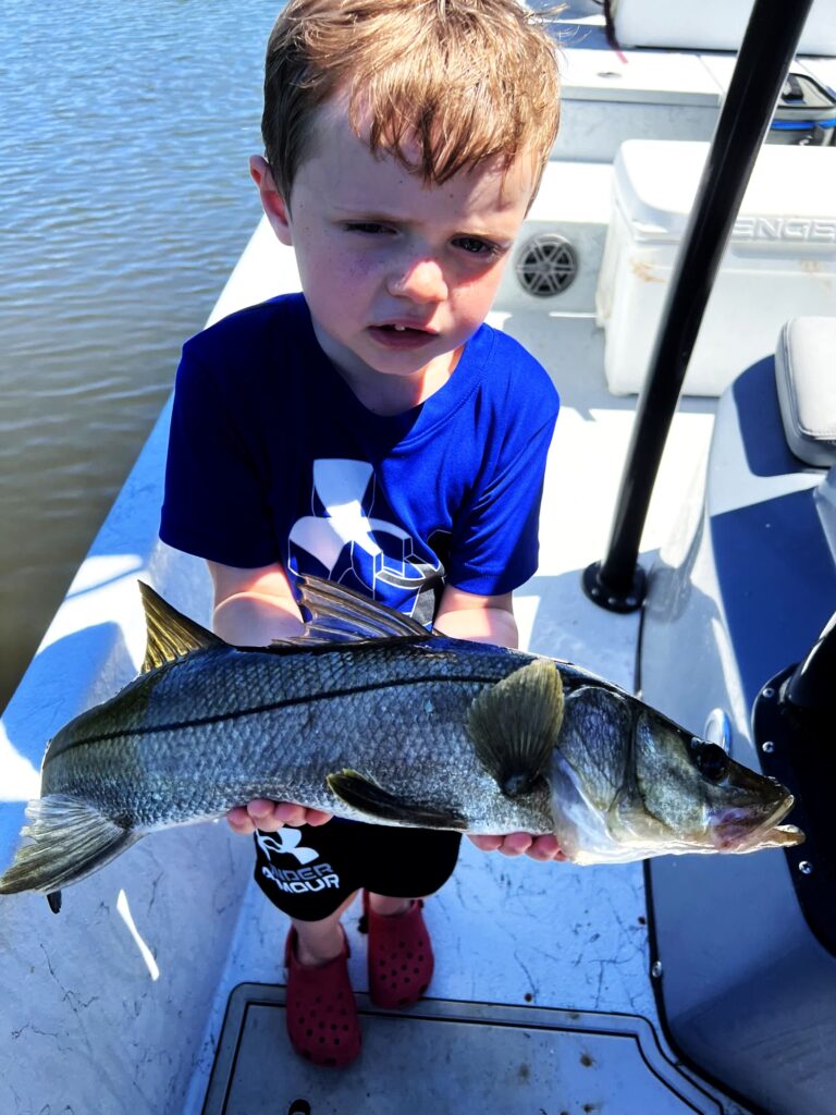 A young angler holding a snook on deck