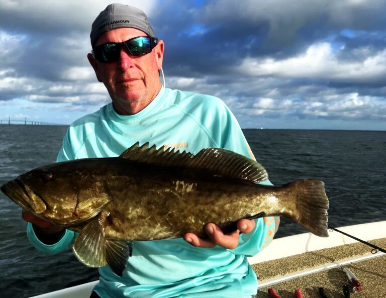 Angler holding a grouper under storm clouds over the bay